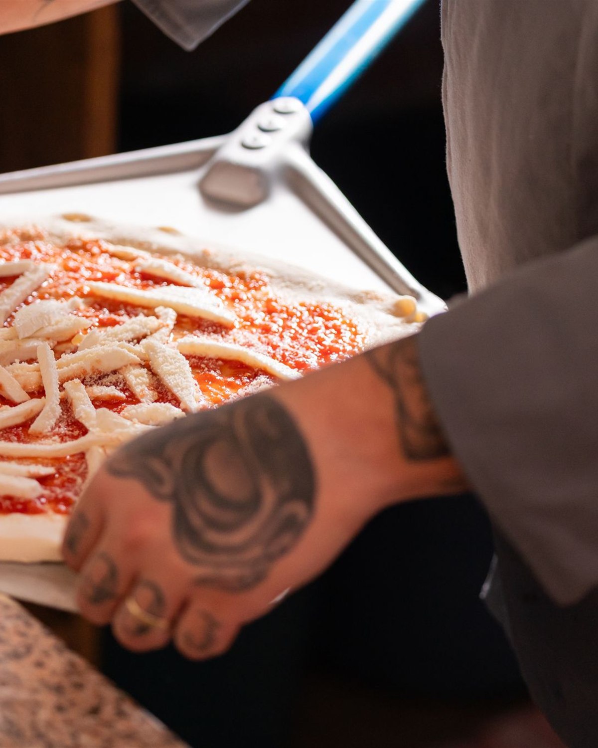 Le mani di un pizzaiolo preparano una base con pomodoro e mozzarella